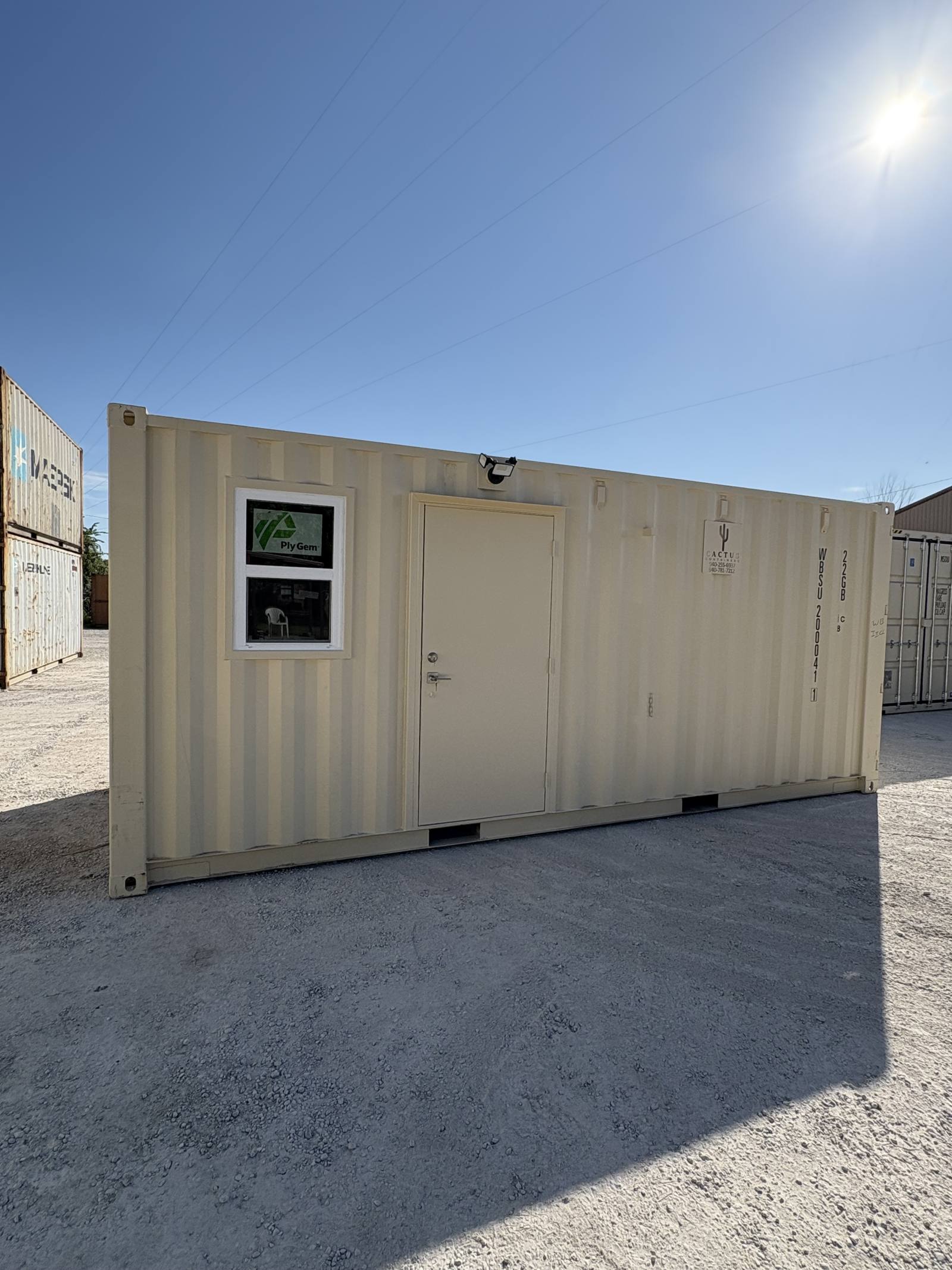 Beige 20-foot shipping container office conversion with a window, personnel door and exterior flood light, on a Cactus Containers yard